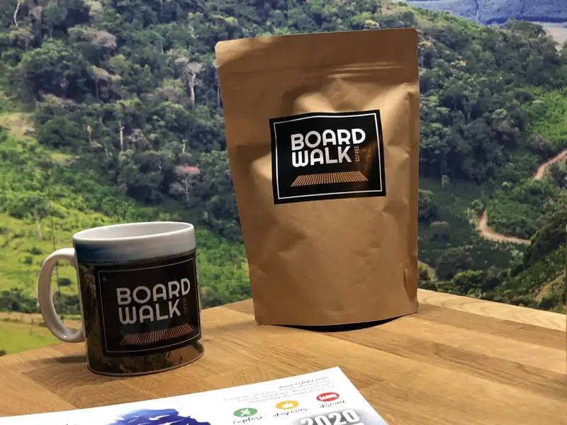 A kraft Boardwalk coffee bag beside a Boardwalk mug on a wooden table.